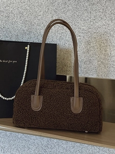 Brown faux shearling underarm bag with leather strap on a decorative wooden shelf