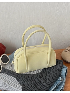 Close-up of pale yellow faux leather bowling bag on casual knitwear and blue jeans