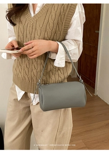 Close-up of a grey litchi-grain leather cylinder bag styled in a soft minimalist setting