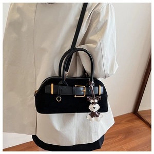Detail view of black suede shoulder bag with gold hardware and dog-shaped charm