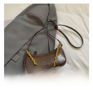 Macro detail of dark brown wax leather baguette bag with gold chain on grey blazer