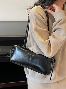 Glossy black baguette shoulder bag with knot details and dual slim straps worn by model