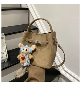 Close-up of khaki litchi grain leather bucket bag with metal lock and cute bear charm