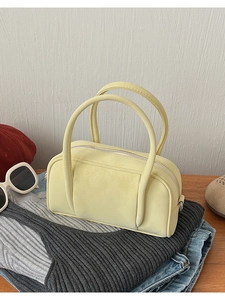 Detail shot of a pale yellow bowling bag with top handles on casual grey knitwear