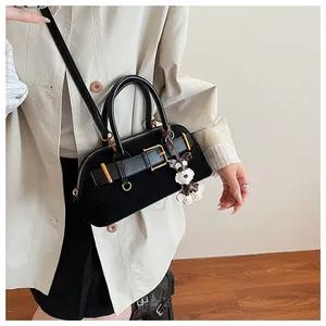 Black suede shell bag worn crossbody with decorative gold buckle and plush dog charm