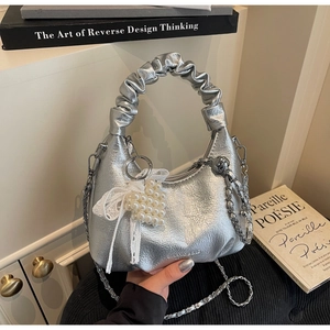 Détail du sac à main argenté avec breloque cœur en dentelle perlée et poignée plissée