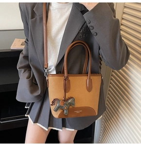 Detalle de un bolso tipo cubo vintage con asa de cuero marrón y colgante de caballo