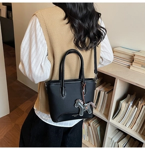 Detalle de bolso tipo cubo en cuero negro con colgante de caballo y bandolera