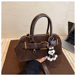Detail of dark brown suede shell bag with leather handles and dog charm accessory