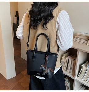 Detalle de bolso tipo cubo en cuero negro con herrajes plateados y colgante de caballo