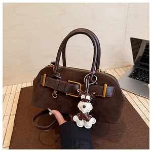 Close-up of brown suede shell bag with dog charm and vintage gold hardware detail