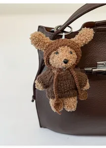Detailed view of a brown plush teddy bear charm with a knitted hoodie on a leather handbag