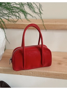 Detailed view of red leather bowling bag with silver zipper on a wooden display