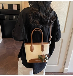 Detalle del bolso tipo cubo de lona y cuero con amuleto de caballo y correa con logo