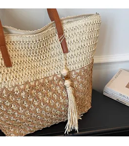 Detail of woven straw tote bag with brown leather handles, tassel charm and zipper closure