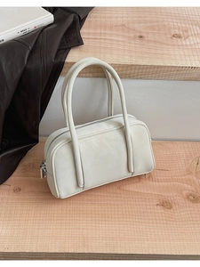 Detail view of a cream white minimalist bowling bag on a light wood background