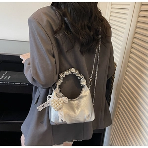 Détail d'un sac à main argenté métallisé avec poignée à volants et breloque cœur perlé