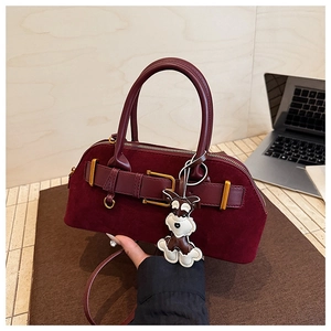 Detail view of a burgundy suede handbag featuring a cute dog charm and adjustable strap