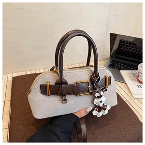 Detail of grey suede shell bag with brown leather straps and cute dog charm on desk