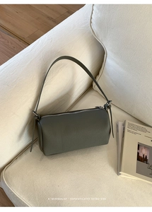 Detail of grey-green cylindrical shoulder bag with litchi grain texture on sofa