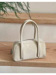 Detail of minimalist off-white bowling handbag with lychee grain texture on wooden shelf