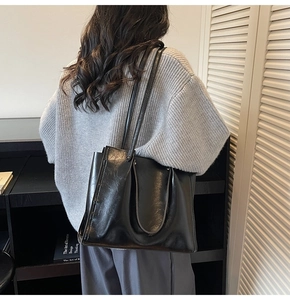 Polished black tote bag side view with dual straps in minimalist library interior