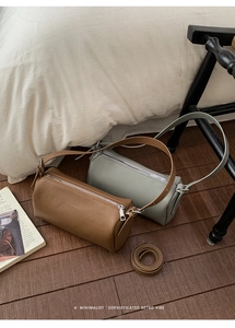 Detail view of cylindrical lychee grain leather bags in brown and grey-blue on wood floor