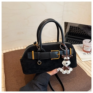 Detail of black suede shell bag with gold buckle and cute puppy charm on felt surface