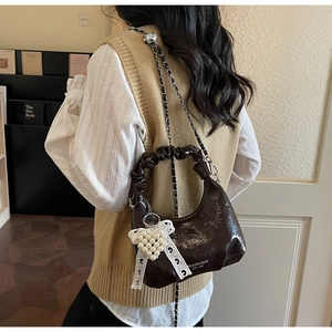 Mini sac bandoulière en cuir verni marron avec chaîne et nœud porté par un modèle