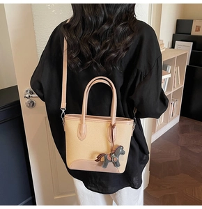 Detalle de bolso tipo cubo de lona bicolor con un colgante de caballo y correa para el hombro