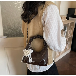 Détail du sac à main en cuir verni marron foncé avec nœud en dentelle et chaîne
