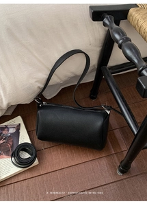 Close-up of black lychee grain leather cylinder bag with silver hardware and detachable strap