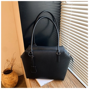 Close-up of black lychee grain leather tote bag with long handles and decorative tag