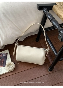 Detail of off-white lychee grain leather pillow bag with silver zipper and dual straps