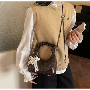 Détail du sac à main en cuir verni marron foncé avec nœud en dentelle et chaîne en métal