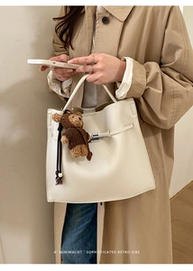 Close-up of white lychee leather handbag with metal buckle and cute bear charm detail