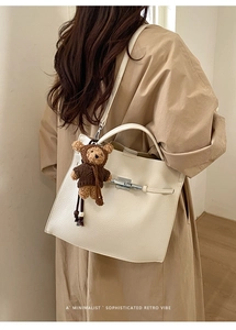 Detail of minimalist cream leather bucket bag with silver clasp and bear charm on model