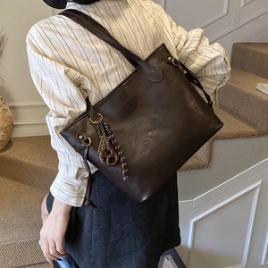 Detail of a large dark brown tote bag with woven pendant and matte leather finish