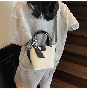 Detail of cream bucket bag with black handle and decorative geometric print silk scarf