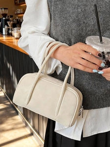 Minimalist beige bowling handbag with tubular handles in a cozy cafe setting