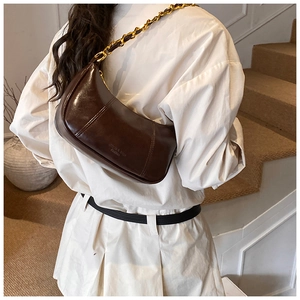 Detail der dunkelbraunen Glanz-Unterarmtasche mit eleganter Goldkette am Modell