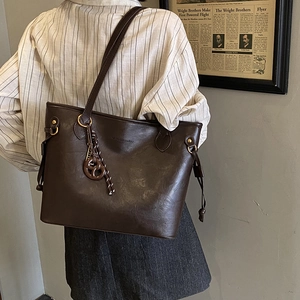 Detail of dark brown leather tote bag showing woven charm and side drawstring texture