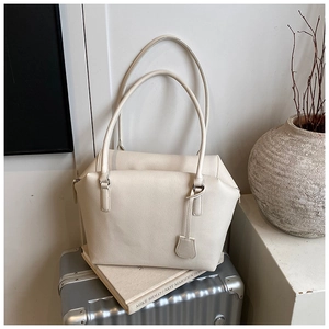 Detail of off-white lychee grain leather tote bag on a suitcase with artistic decor