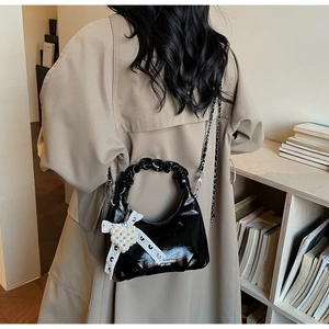 Détail du sac à main en cuir verni noir brillant avec poignée froncée et breloque cœur perle