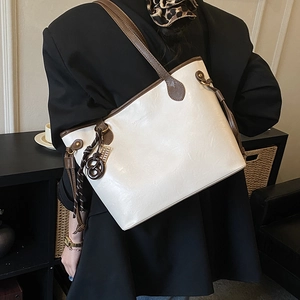Detail of a beige tote bag with brown leather straps and metal charm shown on a model