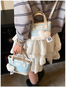Detail of blue plaid bucket bag with plush heart charm and adjustable shoulder strap