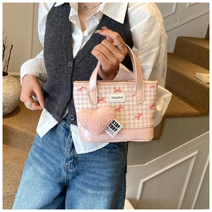 Pink checkered bucket bag detail featuring a plush heart charm and leather handle