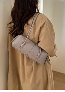 Close-up of a light purple cylindrical shoulder bag with fine stitching on a camel coat