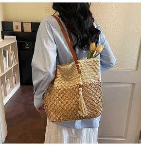 Detail of hollow woven straw beach bag with brown leather handles and fringe charm