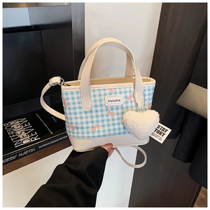 Detail of blue plaid bucket bag featuring pink bow embroidery and heart charm